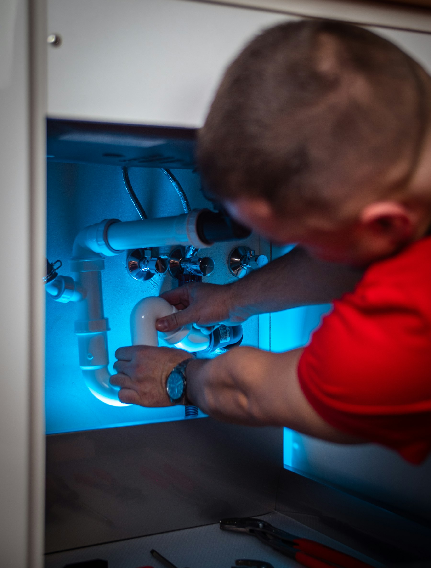 Plumber working on pipes under a sink cabinet